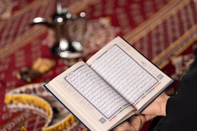 Feelings of reassurance and humility when reciting the Quran, a close-up photo of the hands of a Saudi Arabian Gulf woman wearing a hijab and a black abaya holding the Holy Quran, increasing and striving in worship, getting closer to God in the month of Ramadan, an Emirati woman contemplating and reading verses of the Holy Quran