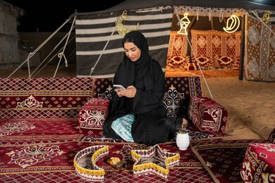 إيماءات السرور والسعادة، الدردشه مع الأهل والأصدقاء، استخدام التكنولوجيا والتقنيات الحديثة المتطورة، امرأة عربية سعودية خليجية محجبة تنظرالي الهاتف، سيده اماراتيه تقوم بالرد على الرسائل النصيه، استخدام التقنيات والاجهزه الحديثه