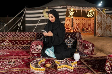 إيماءات السرور والسعادة، الدردشه مع الأهل والأصدقاء، استخدام التكنولوجيا والتقنيات الحديثة المتطورة، امرأة عربية سعودية خليجية محجبة تنظرالي الهاتف، سيده اماراتيه تقوم بالرد على الرسائل النصيه، استخدام التقنيات والاجهزه الحديثه