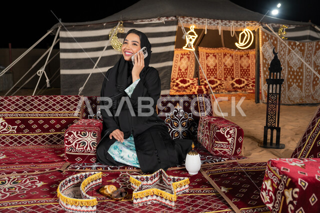Spending enjoyable times exchanging news and conversations, communicating and checking on friends, a veiled Saudi Arabian Gulf woman making a voice call over the phone, an Emirati woman answering calls using a mobile phone, using modern technologies and devices
