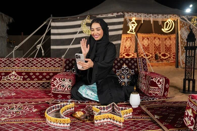 إيماءه الاشاره والترحيب، استخدام الهاتف للدردشه مع الأهل والأصدقاء عبر الانترنت، استخدام التكنولوجيا والتقنيات الحديثة، امرأة عربية سعودية خليجية محجبة تنظرالي الهاتف، سيده اماراتيه تقوم بمكالمه فيديو، استخدام التقنيات والاجهزه الحديثه