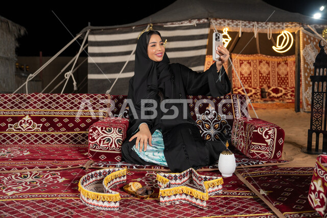 امرأة عربية سعودية خليجية تقوم بإلتقاط صورة سيلفي تذكارية من خلال الجهاز المحمول, توثيق اللحظات السعيدة، إستخدام الأجهزة التقنية الحديثة، سيده اماراتيه تحمل الهاتف المحمول تأخذ صوره تذكاريه، التقدم والتطورالتقني