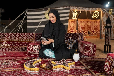 إيماءات السرور والسعادة، الدردشه مع الأهل والأصدقاء، استخدام التكنولوجيا والتقنيات الحديثة المتطورة، امرأة عربية سعودية خليجية محجبة تنظرالي الهاتف، سيده اماراتيه تقوم بالرد على الرسائل النصيه، استخدام التقنيات والاجهزه الحديثه