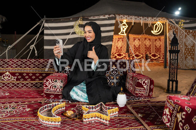 Gesture of greeting, using the phone to chat with family and friends online, using modern technology and techniques, a veiled Saudi Arabian Gulf woman looking at the phone, an Emirati woman making a video call, using modern technologies and devices