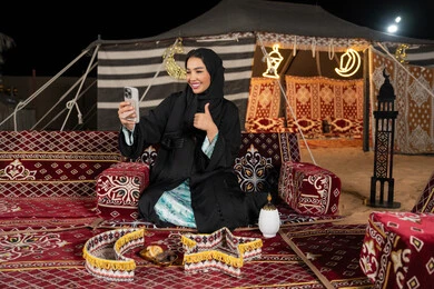 إيماءه الاشاره والترحيب، استخدام الهاتف للدردشه مع الأهل والأصدقاء عبر الانترنت، استخدام التكنولوجيا والتقنيات الحديثة، امرأة عربية سعودية خليجية محجبة تنظرالي الهاتف، سيده اماراتيه تقوم بمكالمه فيديو، استخدام التقنيات والاجهزه الحديثه