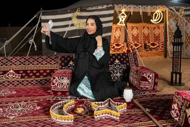 التقاط الصور وتوثيق اللحظات السعيده، سيده اماراتيه ترتدي العباءه السوداء تقوم بالتقاط صوره سيلفي، امرأه عربيه خليجيه سعوديه مبتسمه تقوم باستخدام الهاتف المحمول, المجلس الشعبي التقليدي، التقدم التقني للاجهزه، ديكورات شهر رمضان المبارك