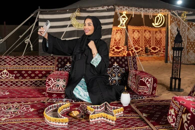 التقاط الصور وتوثيق اللحظات السعيده، سيده اماراتيه ترتدي العباءه السوداء تقوم بالتقاط صوره سيلفي، امرأه عربيه خليجيه سعوديه مبتسمه تقوم باستخدام الهاتف المحمول, المجلس الشعبي التقليدي، التقدم التقني للاجهزه، ديكورات شهر رمضان المبارك
