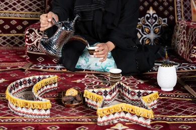 حسن الاستقبال وكرم الضيافه عند العرب،  سيده اماراتيه ترتدي العباءه السوداء تقوم بصب القهوه, المجلس الشعبي التقليدي، صوره مقربه ليدين امرأه عربيه خليجيه سعوديه تحمل الدله النحاسيه وكوب القهوه الساخنه ، ديكورات شهر رمضان الفضيل