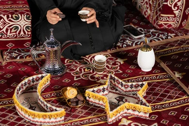 كسر الصيام بتناول حبه التمربجانب القهوه، سيده اماراتيه ترتدي العباءه السوداء تجلس في خيمه وقت الافطار, المجلس الشعبي التقليدي، صوره مقربه ليدين امرأه عربيه خليجيه سعوديه تمسك حبه التمر وكوب القهوه، حسن الاستقبال وكرم الضيافه عند العرب