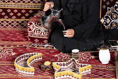 حسن الاستقبال وكرم الضيافه عند العرب،  سيده اماراتيه ترتدي العباءه السوداء تقوم بصب القهوه, المجلس الشعبي التقليدي، صوره مقربه ليدين امرأه عربيه خليجيه سعوديه تحمل الدله النحاسيه وكوب القهوه الساخنه ، ديكورات شهر رمضان الفضيل