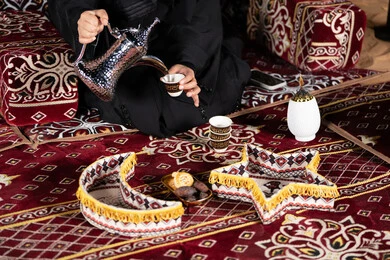 حسن الاستقبال وكرم الضيافه عند العرب،  سيده اماراتيه ترتدي العباءه السوداء تقوم بصب القهوه, المجلس الشعبي التقليدي، صوره مقربه ليدين امرأه عربيه خليجيه سعوديه تحمل الدله النحاسيه وكوب القهوه الساخنه ، ديكورات شهر رمضان الفضيل