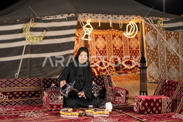 قيم وعادات الضيافه العربيه، حسن الاستقبال وكرم الضيافه،  سيده اماراتيه ترتدي العباءه السوداء تقوم بصب القهوه، امرأه عربيه خليجيه سعوديه مبتسمه تحمل الدله النحاسيه وكوب القهوه, المجلس الشعبي التقليدي