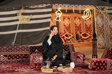 Making a phone call with someone, Emirati woman wearing black abaya making a call to friends, smiling Saudi Arabian Gulf woman using mobile phone, traditional folk council, technical advancement of devices, remote communication, Ramadan decorations