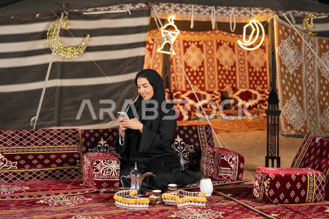 الدردشه والمحادثات النصيه والتواصل عن بعد، سيده اماراتيه ترتدي العباءه السوداء تقوم باجراء مكالمه فيديو مع الاصدقاء، امرأه عربيه خليجيه سعوديه مبتسمه تقوم باستخدام الهاتف المحمول, المجلس الشعبي التقليدي، التقدم التقني للاجهزه، التواصل عبرالانترنت