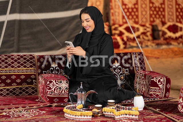 Chatting, texting, and remote communication. An Emirati woman wearing a black abaya is making a video call with friends. A smiling Saudi Arabian Gulf woman is using a mobile phone. Traditional popular council. Technical progress of devices. Communication via the Internet.