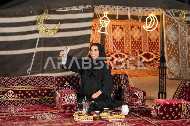 التقاط الصور وتوثيق اللحظات السعيده، سيده اماراتيه ترتدي العباءه السوداء تقوم بالتقاط صوره سيلفي، امرأه عربيه خليجيه سعوديه مبتسمه تقوم باستخدام الهاتف المحمول, المجلس الشعبي التقليدي، التقدم التقني للاجهزه، ديكورات شهر رمضان المبارك