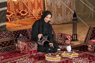Habits inherited from ancestors to serve coffee, an Emirati woman wearing a black abaya holding a copper coffee pot and a cup of coffee, a Saudi Arabian Gulf woman sitting in a tent serving hot coffee, night camping, traditional folk council, generous hospitality and warm welcome
