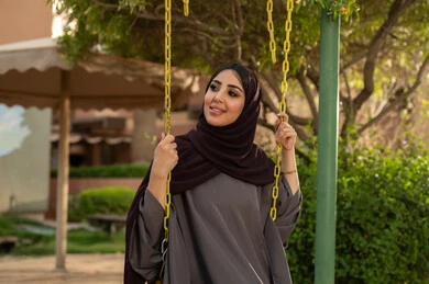 قضاء اوقات سعيده فى الخارج ، بناء علاقات اجتماعية ناجحة  ،الاستمتاع بعطلة نهاية الأسبوع برفقة الأصدقاء في المطاعم والكافيهات، امراه عربيه خليجيه سعوديه  ترتدي العباءه والحجاب تجلس على المرجيحة باحدي الحدائق الترفهيه بالسعودية ،تقوم بتبادل الاحاديث في الأجواء الصيفية اللطيفة ، نزهة في الهواء الطلق