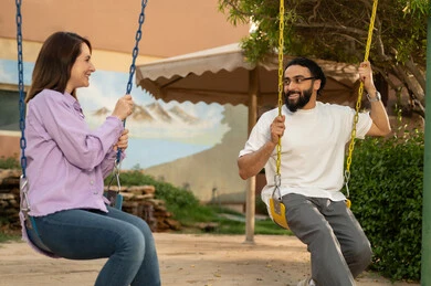 Exchanging conversations between families and colleagues, building successful social relationships, enjoying the weekend with friends, a Saudi Arabian couple sitting on a swing in one of the amusement parks in Saudi Arabia, exchanging talks in the pleasant summer atmosphere, a picnic in the open air.