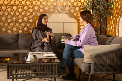 Enjoying the weekend with friends at restaurants and cafes, building successful social relationships and exchanging conversations between families and colleagues, two Arab Gulf friends from Saudi Arabia spend enjoyable evening gatherings in the pleasant summer atmosphere, having refreshing cold drinks outdoors.