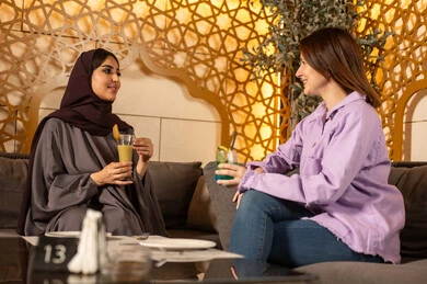 بناء علاقات اجتماعية ناجحة وتبادل أطراف الحديث بين العائلات والزملاء، الاستمتاع بعطلة نهاية الأسبوع برفقة الأصدقاء في المطاعم والكافيهات، صديقتان عربيتان خليجيتان سعوديتان يقضون السهرات المسائية الممتعة في الأجواء الصيفية اللطيفة ، تناول المشروبات الباردة المنعشة  في الهواء الطلق