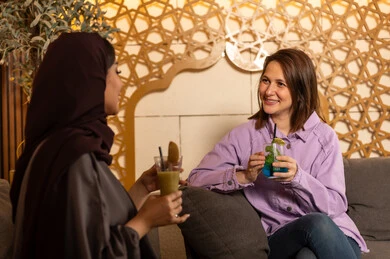 تبادل أطراف الحديث بين العائلات والزملاء، الاستمتاع بعطلة نهاية الأسبوع برفقة الأصدقاء في المطاعم والكافيهات، صديقتان عربيتان خليجيتان سعوديتان يقضون السهرات المسائية الممتعة في الأجواء الصيفية اللطيفة ، تناول المشروبات الباردة المنعشة  في الهواء الطلق