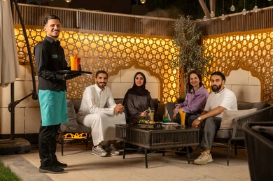 الاستمتاع بعطلة نهاية الأسبوع برفقة الأصدقاء في المطاعم والكافيهات، نادل يرتدي زي اليونيفورم يقوم بتقديم الطلبات ،بناء علاقات اجتماعية ناجحة وتبادل أطراف الحديث بين العائلات والزملاء، مجموعة اصدقاء عرب خليجيين سعوديين يقضون السهرات المسائية الممتعة في الأجواء الصيفية اللطيفة ، تناول المشروبات الباردة المنعشة  في الهواء الطلق