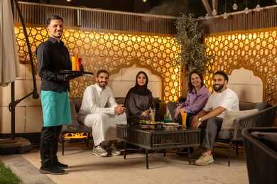 نادل يرتدي زي اليونيفورم يقوم بتقديم الطلبات ،بناء علاقات اجتماعية ناجحة وتبادل أطراف الحديث بين العائلات والزملاء، الاستمتاع بعطلة نهاية الأسبوع برفقة الأصدقاء في المطاعم والكافيهات،مجموعة اصدقاء عرب خليجيين سعوديين يقضون السهرات المسائية الممتعة في الأجواء الصيفية اللطيفة ، تناول المشروبات الباردة المنعشة  في الهواء الطلق