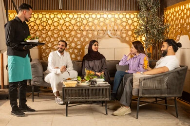 Enjoying refreshing cold drinks outdoors, spending the weekend with friends at restaurants and cafes, a waiter in a uniform serving orders, building successful social relationships and exchanging conversations between families and colleagues, a group of Saudi Gulf Arab friends spending enjoyable evening gatherings in the pleasant summer atmosphere.