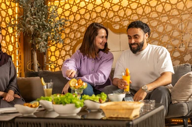 تناول المشروبات الباردة المنعشة  في الهواء الطلق،بناء علاقات اجتماعية ناجحة وتبادل أطراف الحديث بين العائلات والزملاء، الاستمتاع بعطلة نهاية الأسبوع برفقة الأصدقاء في المطاعم والكافيهات،  زوجان عربيان خليجيان سعوديان يقضون السهرات المسائية الممتعة في الأجواء الصيفية اللطيفة