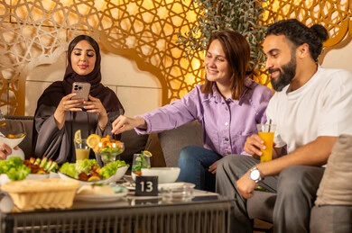 Enjoying the weekend with friends at restaurants and cafes, using mobile phones, exchanging conversations between families and colleagues, a group of Arab Gulf Saudi friends spending enjoyable evening gatherings in the pleasant summer atmosphere, having refreshing cold drinks outdoors.