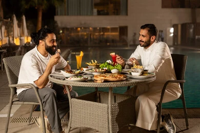 قضاء وقت ممتع مع الأسرة، جلسة عائلية سعيدة,مائدة مليئة بالأطعمة والمشروبات الشهية,  صديقان  عربيان سعوديان خليجيان مبتسمان  يجلسان في مطعم, الاستمتاع بتناول الطعام, حوارات ونقاشات على مائدة الطعام