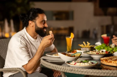 مائده مليئه بأصناف المأكولات و المقبلات الشهية، مأكولات عربيه وصفات شهيه  , صورة من الجانب لرجل عربي خليجي سعودي يرتدي الزي الكاجوال  يقوم بتناول الطعام