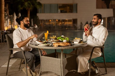 مائدة مليئة بالأطعمة والمشروبات الشهية, قضاء وقت ممتع مع الأسرة، جلسة عائلية سعيدة, صديقان  عربيان سعوديان خليجيان مبتسمان  يجلسان في مطعم, الاستمتاع بتناول الطعام, حوارات ونقاشات على مائدة الطعام