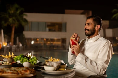 A side view of a Saudi Arabian Gulf man wearing traditional attire eating food, with Arabic dishes and delicious recipes, a table filled with various dishes and tasty appetizers.