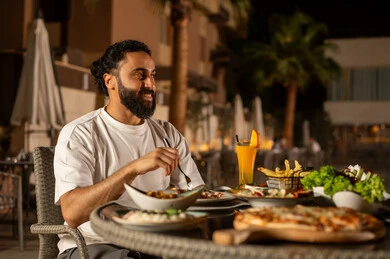 مأكولات عربيه وصفات شهيه  , صورة من الجانب لرجل عربي خليجي سعودي يرتدي الزي الكاجوال  يقوم بتناول الطعام , مائده مليئه بأصناف المأكولات و المقبلات الشهية