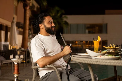 رجل عربي خليجي سعودي يجلس في الهواء الطلق، القيام بنشاطات ممتعة بعطلة نهاية الأسبوع، تدخين الشيشة وتناول المشروبات الباردة، جلسة وناسة وتسلية في أجواء صيفية لطيفة،ارتياد المطاعم والمقاهي في المملكة العربية السعودية