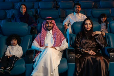 A fantastic cinematic experience, an Arab Saudi Gulf audience in a cinema hall, a four-dimensional screening room, modern display technologies, advanced audio, visual, and sensory cinematic effects, enjoying popcorn, facial expressions indicating joy and happiness, a family entertainment activity.