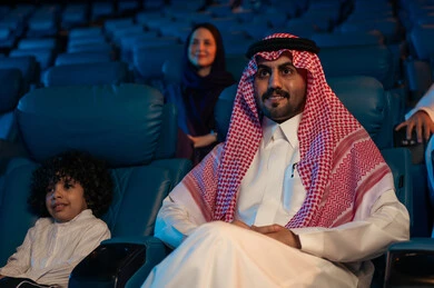 Advanced cinematic audio, visual, and sensory effects, an Arab Saudi Gulf audience in a cinema hall, a four-dimensional screening room, modern display technologies, a fantastic cinematic experience, enjoying popcorn, facial expressions indicating joy and happiness, a family entertainment activity.