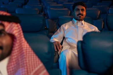 أنشطة ترفيهية سعيدة، قضاء أوقات ممتعة، رجل عربي سعودي خليجي  في صالة السينما، تعابير تدل على الإندماج، الإستمتاع بتناول الفشار والمشروبات الباردة ، مشاهدة الأفلام والعروض المسرحية في السينما، سينما ومسرح، خلفية قاعة عرض السينما، صالة العرض