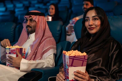 Facial expressions indicating joy and happiness, a family entertainment activity, an Arab Saudi Gulf audience in a cinema hall, a four-dimensional screening room, modern display technologies, advanced audio, visual, and sensory cinematic effects, a fantastic cinematic experience, enjoying eating popcorn.