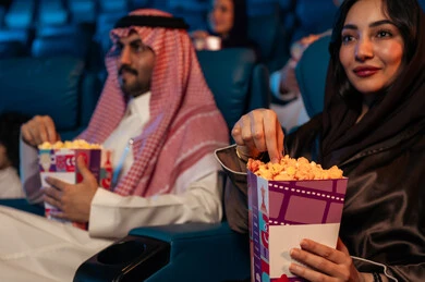 A family entertainment activity, an Arab Saudi Gulf audience in a cinema hall, a four-dimensional screening room, modern display technologies, advanced audio, visual, and sensory cinematic effects, a fantastic cinematic experience, enjoying popcorn, facial expressions indicating joy and happiness.