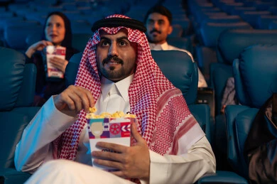 أنشطة ترفيهية سعيدة، قضاء أوقات ممتعة، رجل عربي سعودي خليجي في صالة السينما، تعابير تدل على الإندماج، الإستمتاع بتناول الفشار والمشروبات الباردة ، مشاهدة الأفلام والعروض المسرحية في السينما، سينما ومسرح، خلفية قاعة عرض السينما، صالة العرض