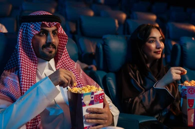 مشاهدة الأفلام والعروض المسرحية في السينما، أنشطة ترفيهية سعيدة، قضاء أوقات ممتعة، رجل عربي سعودي خليجي بجانب زوجته في صالة السينما، تعابير تدل على الإندماج، الإستمتاع بتناول الفشار والمشروبات الباردة ،  سينما ومسرح، خلفية قاعة عرض السينما، صالة العرض