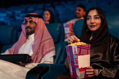 المؤثرات الصوتيه والبصريه والحسيه السينمائيه المتطوره, تجربه سينمائيه خياليه، جمهور عربي سعودي خليجي في صالة سينما، صالة عرض رباعية الأبعاد, تقنيات العرض الحديثه,  الاستمتاع بأكل الفشار، تعابير وجه تدل على الفرح والسعاده, نشاط عائلي ترفيهي