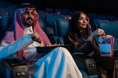 أنشطة ترفيهية سعيدة، قضاء أوقات ممتعة، رجل عربي سعودي خليجي بجانب زوجته في صالة السينما، تعابير تدل على الإندماج، الإستمتاع بتناول الفشار والمشروبات الباردة ، مشاهدة الأفلام والعروض المسرحية في السينما، سينما ومسرح، خلفية قاعة عرض السينما، صالة العرض