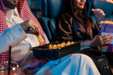 تعابير تدل على الإندماج، صورة مقربة للمقرمشات ذهبية اللون ،أنشطة ترفيهية سعيدة، قضاء أوقات ممتعة، جمهور عربي سعودي خليجي  في صالة السينما، مشاهدة الأفلام والعروض المسرحية في السينما، سينما ومسرح، خلفية قاعة عرض السينما، صالة العرض