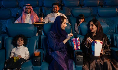 جمهور عربي سعودي خليجي في صالة سينما، صالة عرض رباعية الأبعاد, تقنيات العرض الحديثه, المؤثرات الصوتيه والبصريه والحسيه السينمائيه المتطوره, تجربه سينمائيه خياليه، الاستمتاع بأكل الفشار، تعابير وجه تدل على الفرح والسعاده, نشاط عائلي ترفيهي