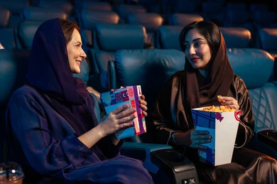 الاستمتاع بتناول الفشار ، مشاهدة الأفلام والمسرحيات والعروض المتنوعة,شاشات ضوئية كبيرة لزيادة الاستمتاع بالتجربة، القيام بنشاطات ترفيهية ممتعة, صديقتان عربيتان خليجيتان سعوديتان تجلسان في قاعة السينما وتتابعان الفيلم بايماءات السعادة, دور العرض الحديثة في المملكة العربية السعودية