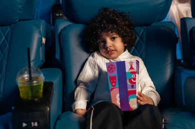 ولد عربي خليجي سعودي في صالة السينما، تعابير تدل على الإندماج، الإستمتاع بتناول الفشار، قضاء أوقات ممتعة، أنشطة ترفيهية، مشاهدة الأفلام والعروض المسرحية في السينما، سينما ومسرح، خلفية قاعة عرض السينما، صالة العرض